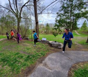 On a lush green lawn with trees, people laugh as they practice Zumba a safe distance apart.