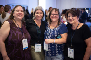 Four women smile while wearing conference badges.