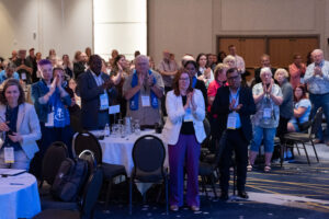 Delegates at a meeting stand and applaud.