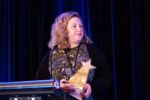 A woman at a podium holds a star-shaped award