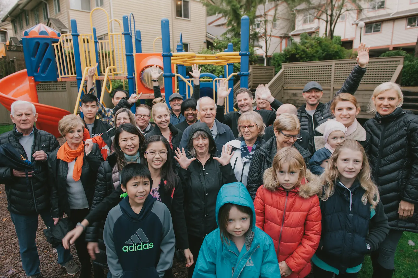 Un groupe diversifié d'adultes et d'enfants se rassemblent et sourient pour une photo devant une structure de jeu colorée dans une coopérative d'habitation, soulignant l'esprit de la FHCC.