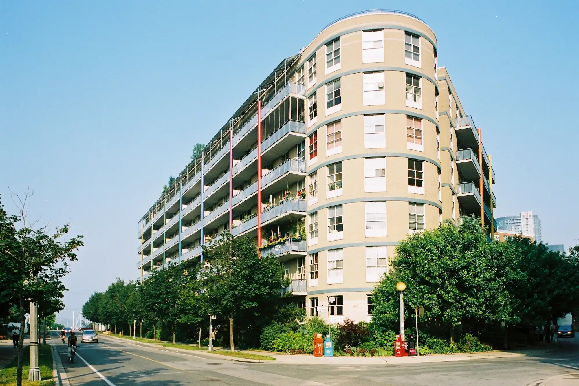 Le long d'une rue calme et bordée d'arbres, par temps clair, un grand immeuble de logements coopératifs aux formes arrondies, avec des balcons et de la verdure.