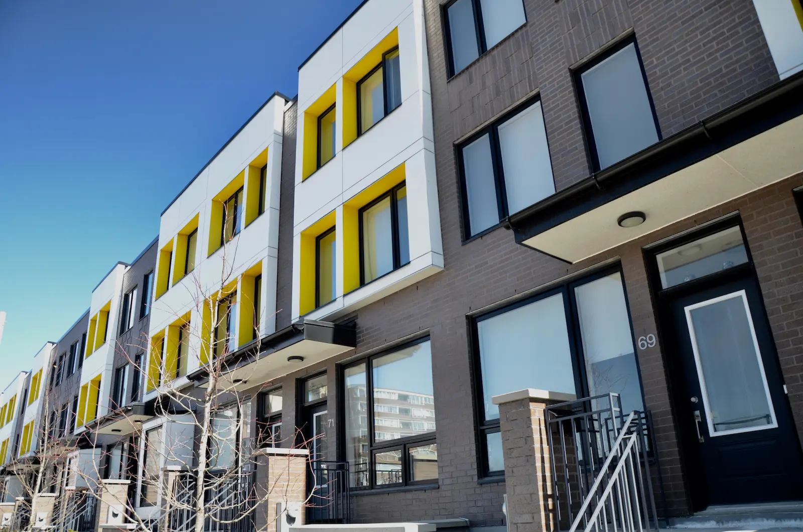 Modern row of multi-story co-operative housing townhouses with large windows, yellow accents, and brick exteriors, viewed from the street on a clear day.