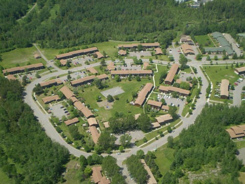 Vue aérienne d'un complexe résidentiel composé de plusieurs bâtiments aux toits bruns, entourés de verdure et de routes - un exemple d'habitation coopérative qui reflète les valeurs soutenues par la FHCC.