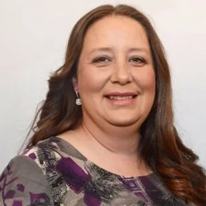 A woman with long brown hair, wearing a patterned top and earrings, smiles at the camera against a plain background—reflecting the welcoming spirit of co-operative housing supported by CHF Canada.
