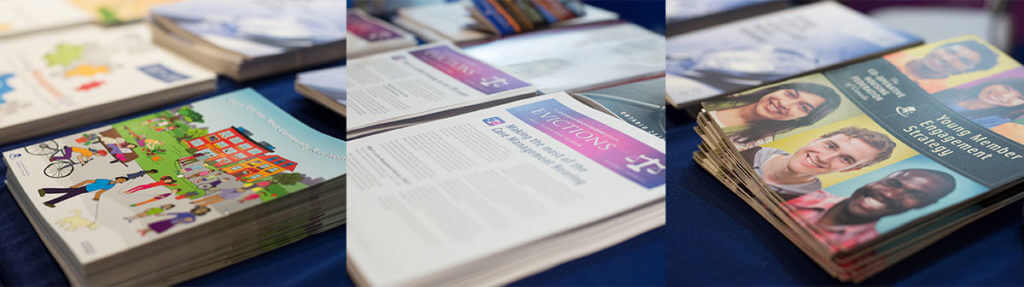 Several stacks of informational brochures and magazines about co-operative housing are arranged on a table, featuring illustrations, articles, and photos of diverse individuals on their covers, some highlighting CHF Canada initiatives.