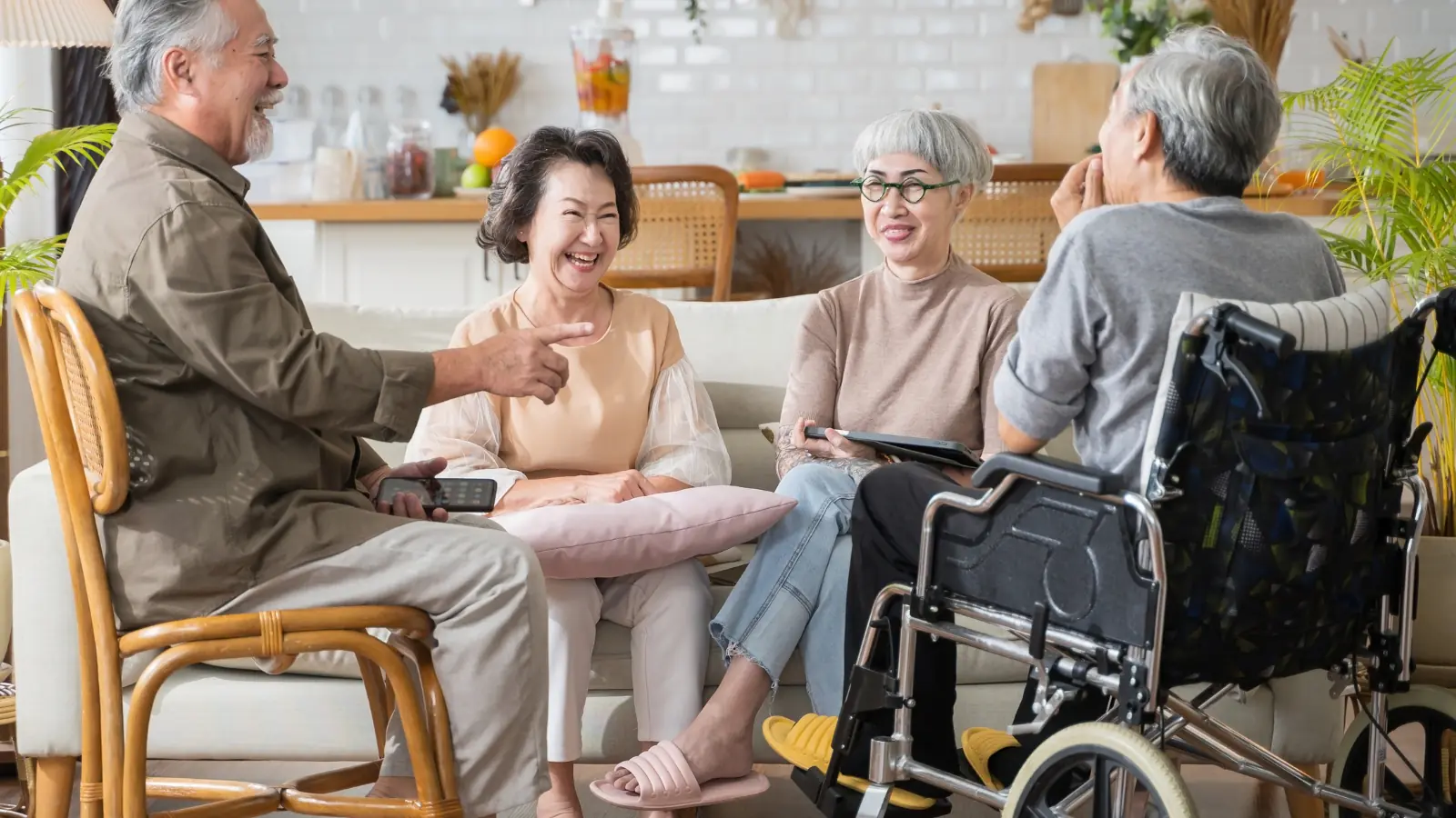 Four older adults sit together in a cozy Co-operative Housing living room, talking and smiling; one person uses a wheelchair.